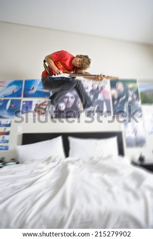 Teenage boy (16-18) playing electric guitar in bedroom in air, smiling, portrait (digital enhancement)