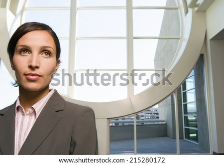 Businesswoman standing in lobby, near large circular window, smiling, front view