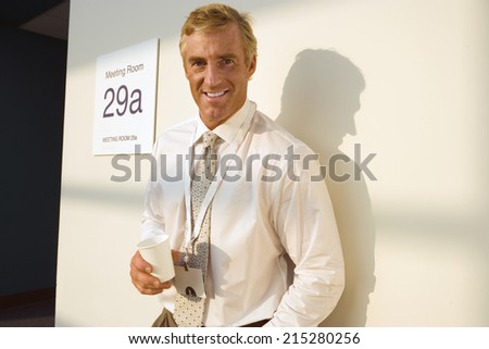 Businessman standing outside meeting room, taking coffee break, casting shadow on wall, smiling, portrait
