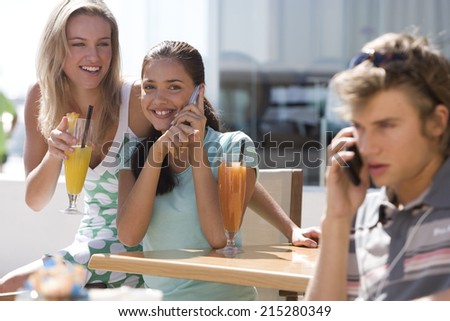 Three friends in cafe outdoors, young man and young woman using mobile phones