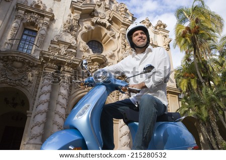 USA, California, San Diego, Balboa Park, man riding on blue motor scooter, smiling, side view, low angle view