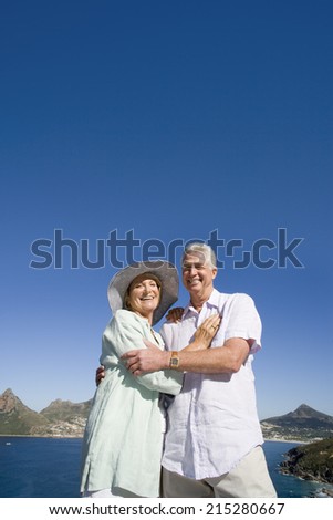 South Africa, Cape Town, senior couple embracing by sea, smiling, portrait, low angle view