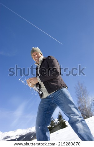 Young man holding snow ball in snow field, smiling, portrait, low angle view