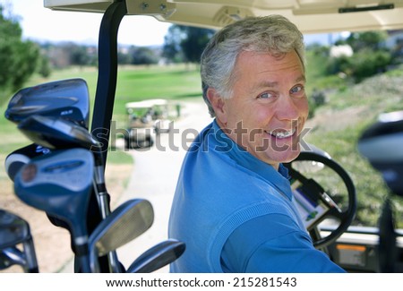 Mature man driving golf buggy on golf course, looking over shoulder, smiling, close-up, rear view, portrait