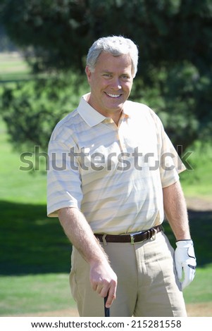 Mature man, in striped short-sleeved shirt and golf glove, standing on golf course, leaning on golf club, smiling, front view, portrait