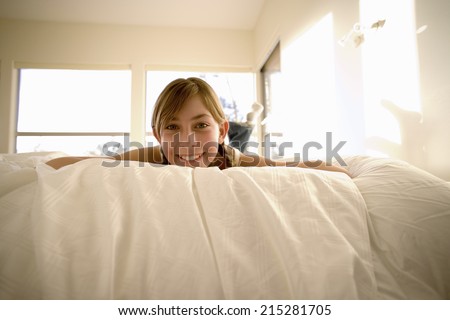 Girl (11-13) lying on front on bed, smiling, portrait, low angle view