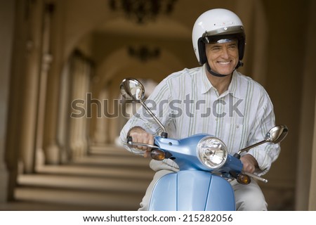 Senior man sitting on motor scooter near colonnade, smiling, front view (tilt)