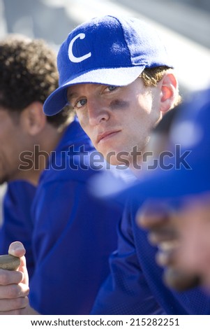 Baseball team sitting in batterÃ?Â¢Ã¢Â?Â¬Ã¢Â?Â¢s box during competitive baseball game, focus on captain wearing blue cap, side view, portrait (differential focus)