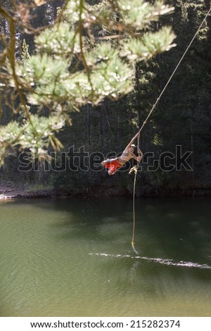 Boy , in swimming shorts, swinging on rope above lake