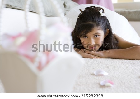 Girl (8-10), in bridesmaidÃ?Â¢Ã¢Â?Â¬Ã¢Â?Â¢s dress, lying face down on carpet in living room, wedding gift in foreground, focus on girl, smiling, front view, portrait (surface level)