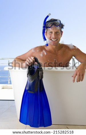 Man wearing snorkle and holding flippers whilst in bubble bath, smiling, portrait