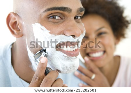 Young woman smiling at man shaving, portrait of man, close-up