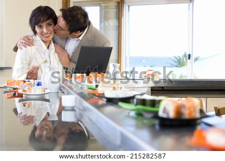 Couple with laptop in sushi bar, man kissing woman