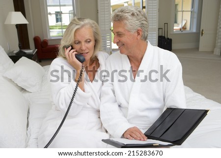 Mature couple sitting on bed, man smiling at woman talking on telephone