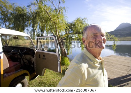Senior man by camper van by lake, smiling, portrait, close-up
