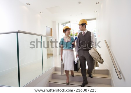 Businessman and woman with briefcases in hard hats on stairs, looking at each other
