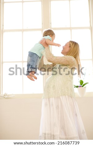 Pregnant woman lifting up baby daughter (9-12 months), smiling, low angle view