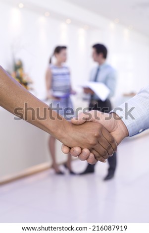 Businessman and woman shaking hands, colleagues in background, close-up of hands