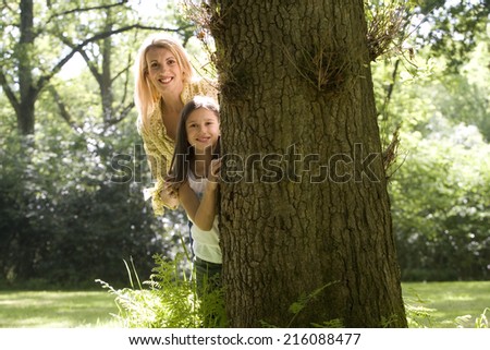 Mother and daughter peeking out from behind tree, low angle view