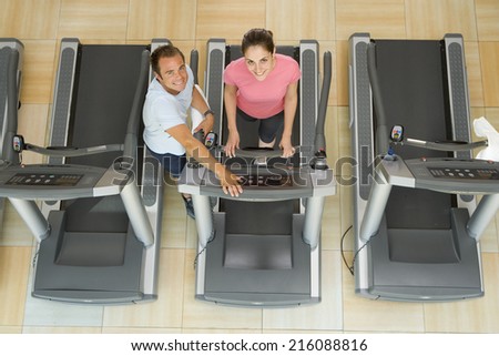 Man helping woman on treadmill in gym, elevated view