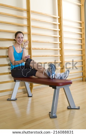 Young woman with MP3 player on exercise horse in gym, smiling, low angle view