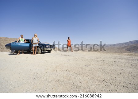 Small group of friends by car in desert, looking at view, low angle view