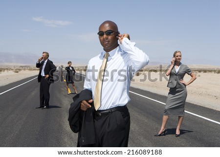 Small group of businessmen and women using mobile phones on road in desert, low angle view