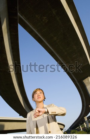 Businesswoman looking at watch beneath overpasses, low angle view