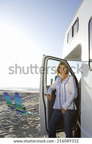 Mature woman getting out of motor home on beach, smiling, portrait