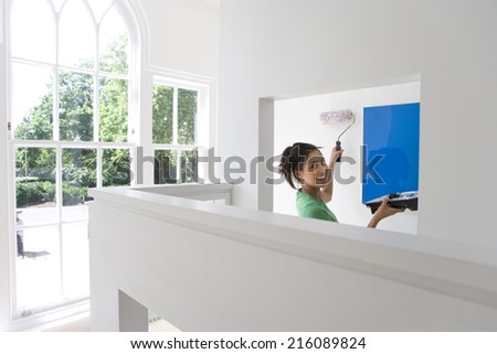 Young woman with tray and roller painting wall, smiling, portrait
