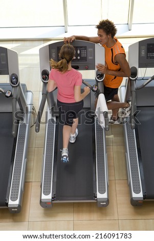 Fitness instructor training woman on treadmill in gym, elevated view