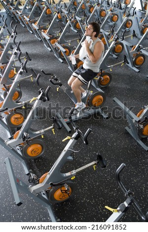 Man with bottle of water on exercise bicycle in gym, using towel, elevated view