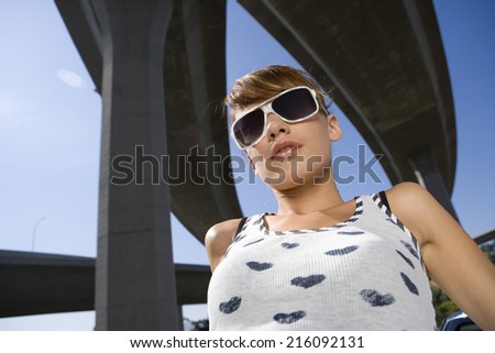 Young woman in sunglasses beneath overpasses, low angle view