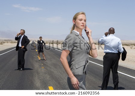 Small group of businessmen and women using mobile phones on road in desert