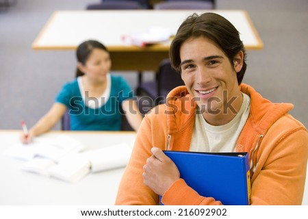 Young man with folder studying in library, smiling, portrait, elevated view