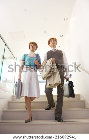 Businessman and woman in hard hats on stairs, low angle view
