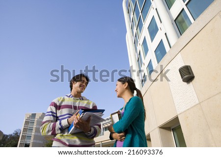 Yound man and woman with books smiling at each other, low angle view