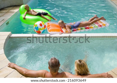Family of four in swimming pool, boy and girl (7-11) on inflatable chair and bed