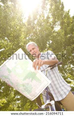 Mature man with bicycle reading map, low angle view (sun flare)