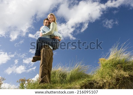 Man holding up woman outdoors, smiling, portrait, low angle view