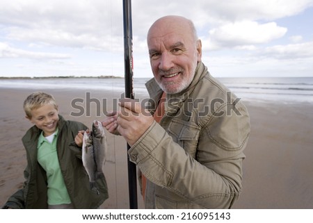 Grandfather and grandson with fishing rod and fish on beach, smiling, portrait