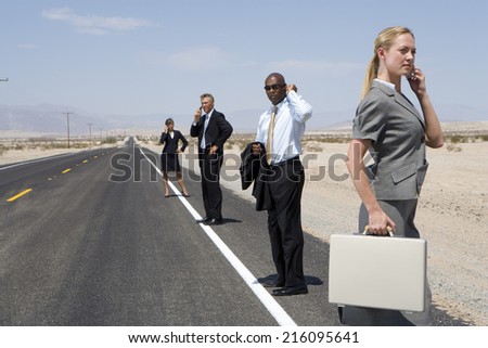 Small group of businessmen and women using mobile phones on side of road in desert, side view