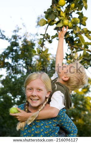 Boy on sister\'s (11-13) back, reaching for apple, portrait of girl smiling