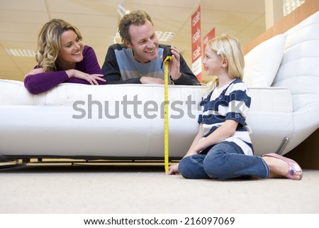 Young couple measuring bed in furniture shop, smiling at daughter (6-8)