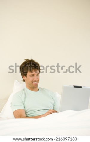 Young man using laptop computer in bed, smiling, close-up