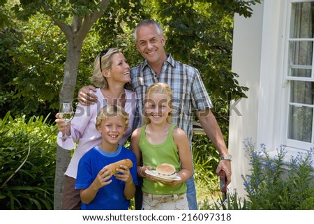 Family of four in garden, woman with glass of wine, boy and girl (8-12) with burgers, smiling, portrait