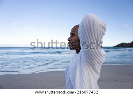 Young man with arms behinid head on beach, side view