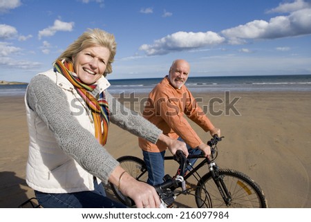 Senior couple cycling on beach, smiling, portrait, side view