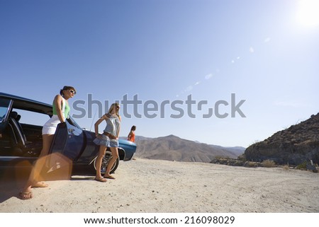 Small group of friends by car in desert, looking at view, low angle view (lens flare)