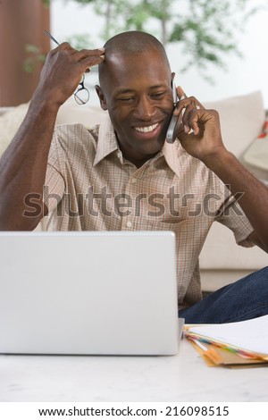 Man on mobile phone at laptop computer, smiling